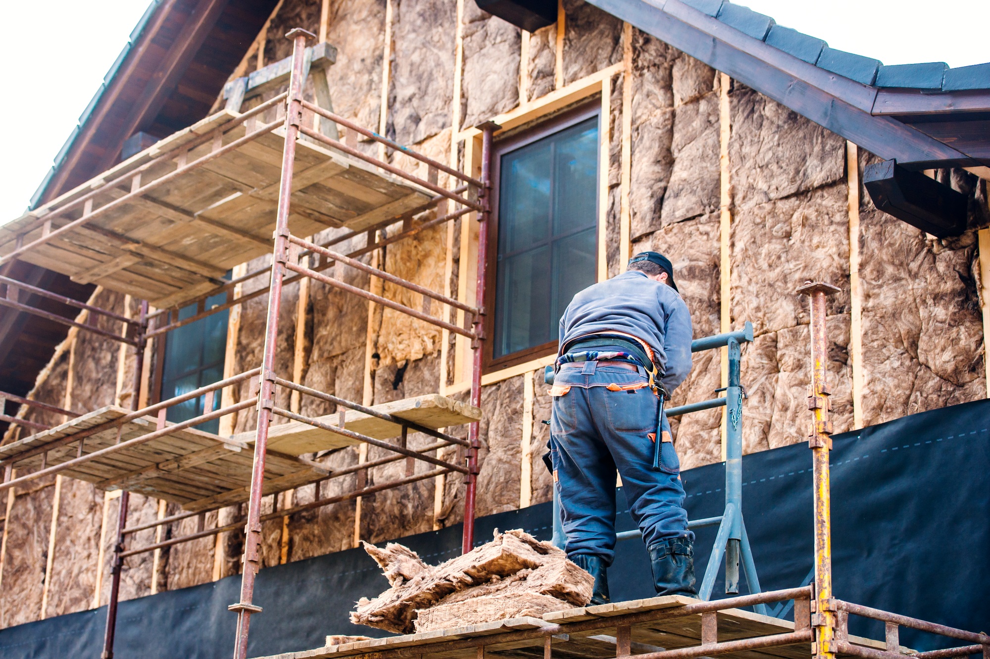 Construction worker thermally insulating house facade with glass wool.